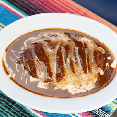 Chicken breast covered in rich mole sauce with a swirl of crema.
