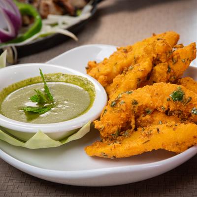 Crispy golden Amritsari fried fish served with green mint chutney on a platter.