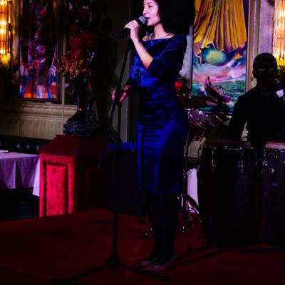 Singer holding the microphone during live music, artwork visible in the background.