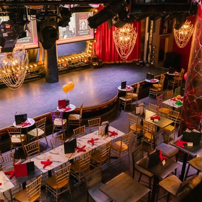 Show room featuring a burlesque stage and seating area with tables and chairs.