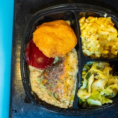 Chicken with dressing, served with mac and cheese, cabbage, and a croquette with red sauce.