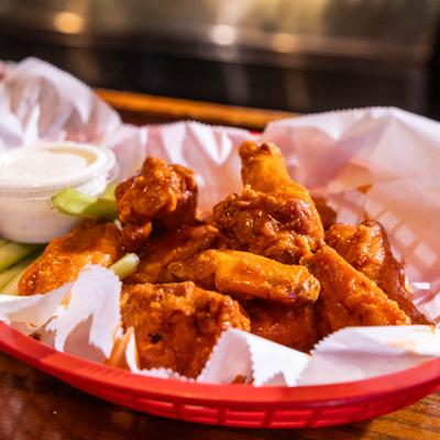 Basket of Buffalo chicken wings served with a side of dipping sauce and celery.