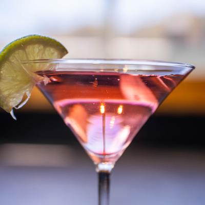 Pink cocktail served in a martini glass, garnished with a slice of lime.