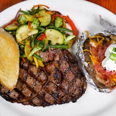 Grilled ribeye steak with, garlic bread, sauteed vegetables, and loaded baked potato.