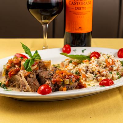 Ossobuco with risotto on a plate, accompanied with red wine.