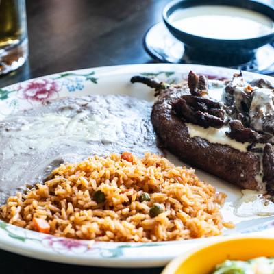 A poblano pepper stuffed with melted cheese, topped with meat, served with rice and beans.
