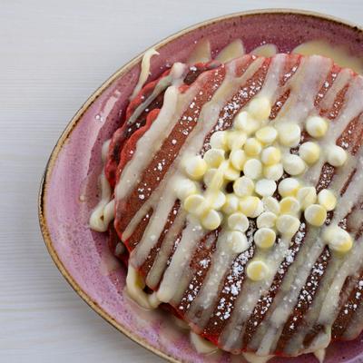 Red velvet pancakes topped with icing, white chocolate chips, and powdered sugar.