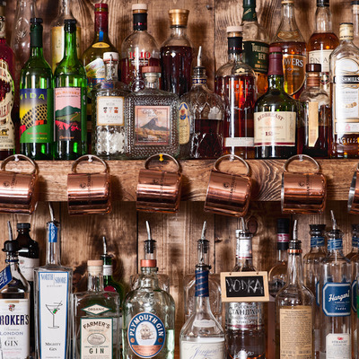 Shelves with bottles of liquor and Moscow Mule copper mugs hanging from hooks.