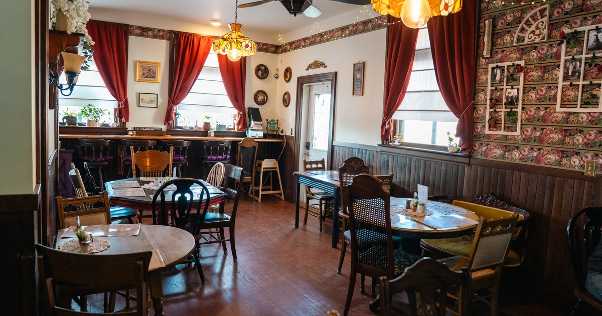 Interior of a vintage-style cafe with red curtains, wooden furniture, floral wallpaper, and stained glass lighting