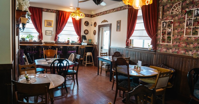 Interior of a vintage-style cafe with red curtains, wooden furniture, floral wallpaper, and stained glass lighting