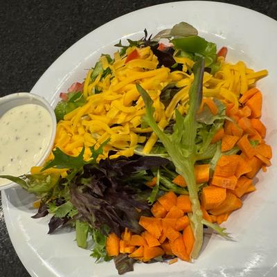Mixed salad with shredded cheese, carrots, and ranch dressing on the side.