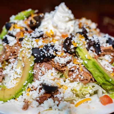 Fried corn tortilla with refried beans, lettuce, tomato, cheese, olives, avocado, and sour cream.