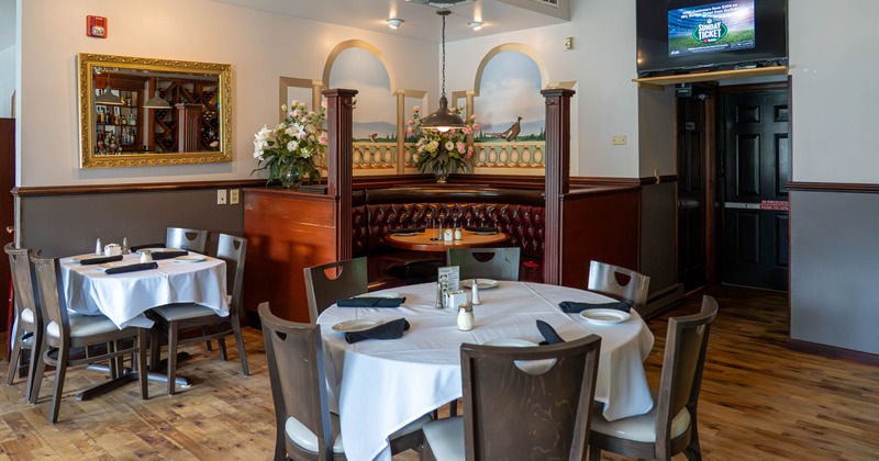 Interior, wooden tables and chairs, white tablecloths, flowers, gold-framed mirror, wall-mounted TV