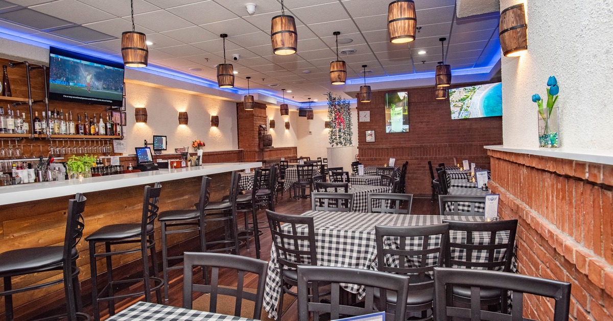 Interior of a restaurant with checkered tablecloths, a bar area, and warm lighting