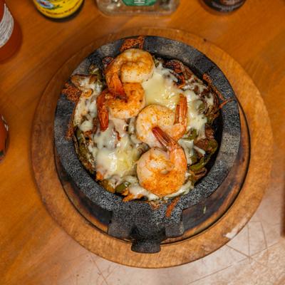 Molcajete bowl with steak, shrimp, chicken, cactus, hot sauce, and melted cheese.