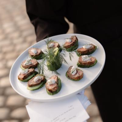 Server holding a plate of smoked salmon cucumber appetizers.