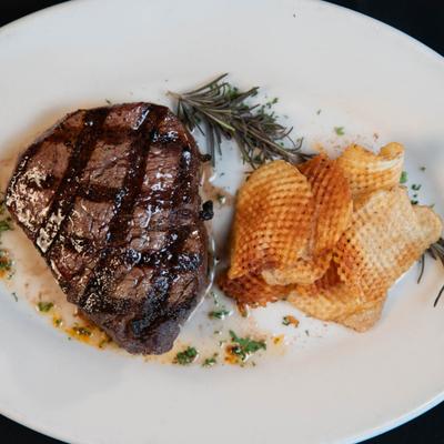 Filet Mignon served alongside a stack of golden waffle fries on a white plate, top view.