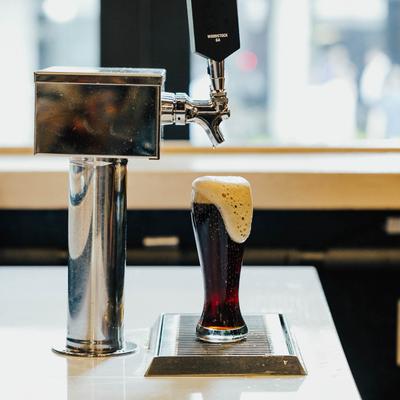 Glass filled with foamy dark beer under a beer tap.