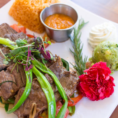 A steak with rice, avocado, and a spread.