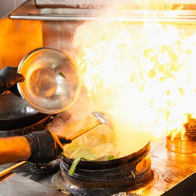 Chef stir-frying vegetables in a flaming wok.
