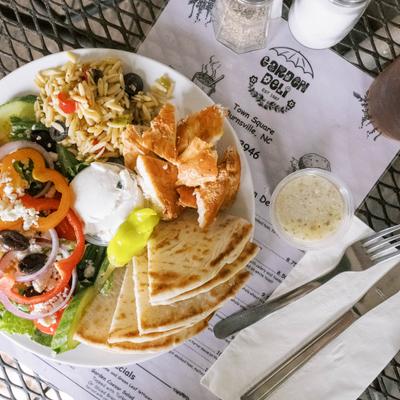 A Greek platter with chicken, pita bread, tzatziki, and fresh Mediterranean side salads.