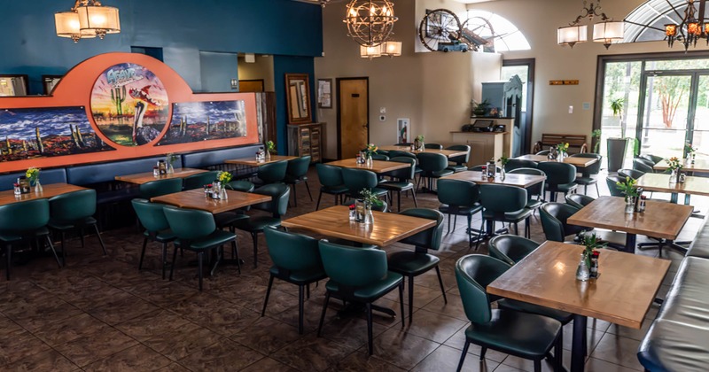 Interior, dining room with wooden tables, teal chairs, hanging lanterns, desert-themed wall art