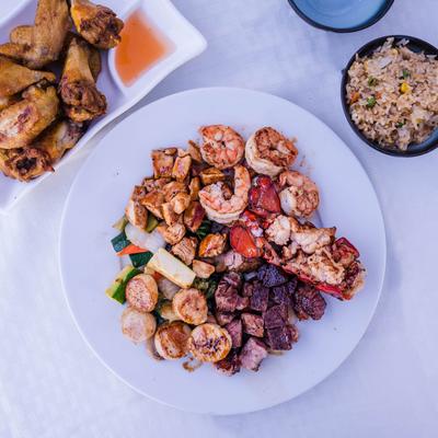 A plate of grilled seafood and meats served with chicken wings and fried rice.