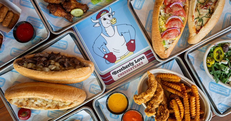 Various comfort food on a table with a menu featuring a cow in boxing gloves and the logo