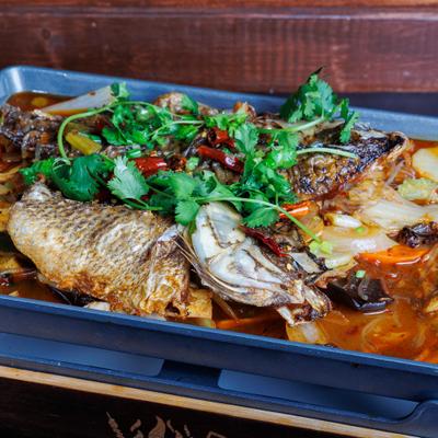 Whole cooked fish in spicy sauce with vegetables and cilantro on a serving tray.