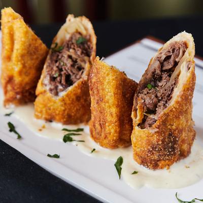 Three crispy egg rolls filled with savory shredded beef, displayed on a white plate