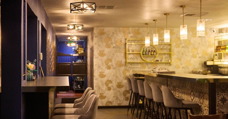 Cozy bar interior with gray chairs, pendant lights, and a decorative wall backdrop