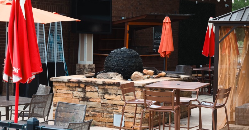 Outdoor patio with tables, chairs, a fountain, umbrellas, string lights, and a bar area