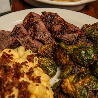 Sliced steak served with bacon-topped mac and cheese and Brussels sprouts.