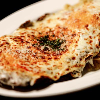 Chicken Parmigiana topped with melted cheese and herbs, close-up.