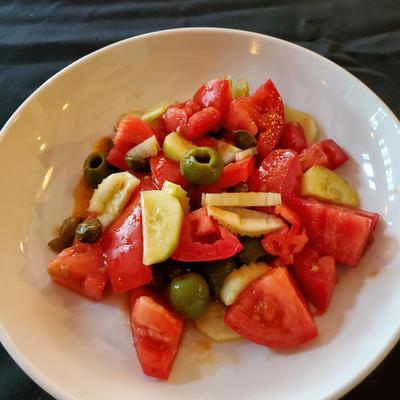 Tomato and cucumber salad with olives in a white bowl.