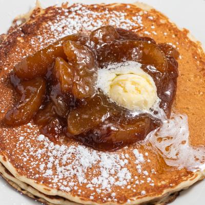 Buttermilk pancakes topped with apples in a cinnamon butter sauce, dusted with powdered sugar.