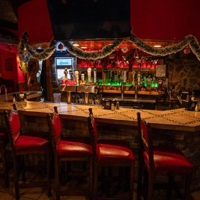 A cozy bar with a stone counter adorned with red chairs and festive garland.