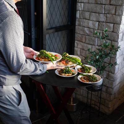 Person carrying plated meals to a table beside a stone wall.