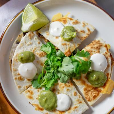 Quesadilla slices topped with crema and guacamole, served with lime  and cilantro, lime.