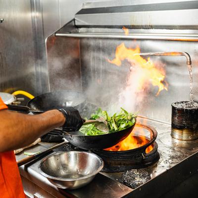Chef stir-frying greens in a flaming wok.