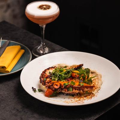 Grilled octopus vith various garnishes, served alongside Blackberry Martini.