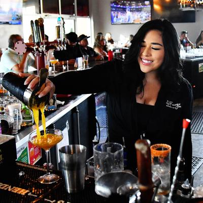 A bartender pouring a cocktail from a shaker into a coupe glass.