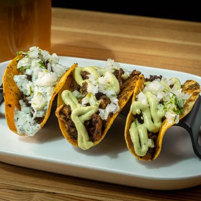 Three distinct tacos served in a white oval dish using black taco holder.