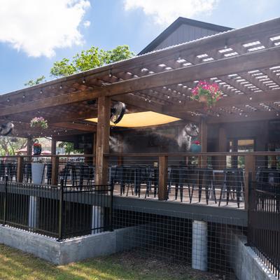 Outdoor wooden patio with pergola, hanging plants, seating, and misting fans.
