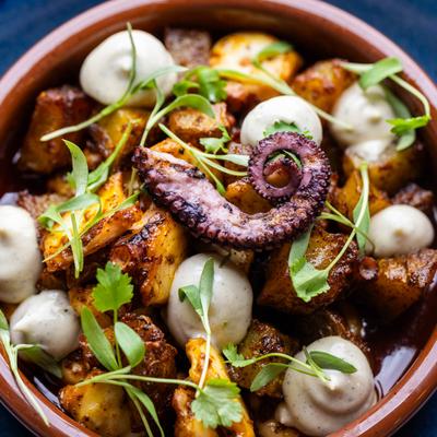 Close-up of grilled octopus with seasoned potatoes and herb garnish.