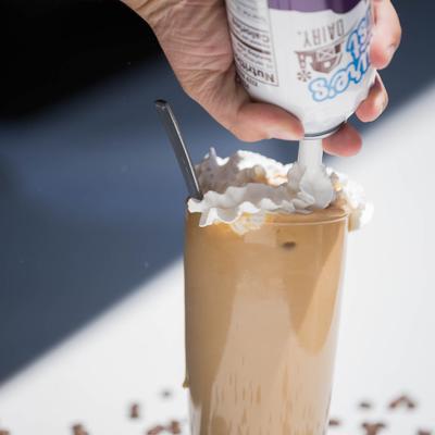 A server adds whipped cream to latte coffee, close up.