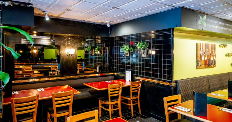 Interior - red tables, wooden chairs, black tile walls and decorative plants.