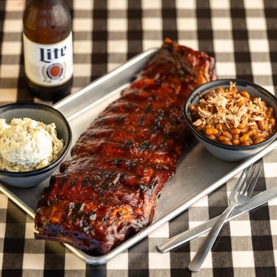 Full slab of BBQ ribs, with baked beans, and potato salad on the side.