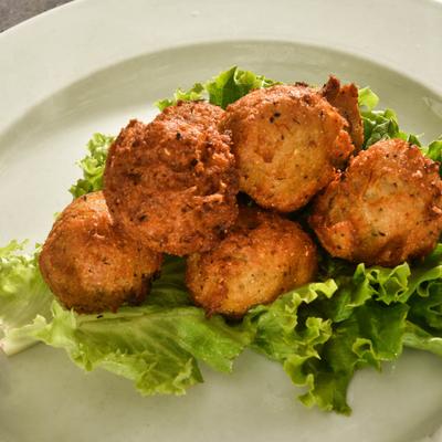 New England Golden Brown Hush Puppies stacked on fresh lettuce, on a white plate.