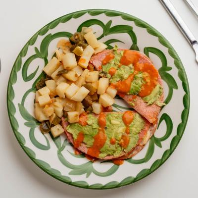 Ham and cheese tortilla melt with avocado spread, red salsa, and breakfast potatoes.